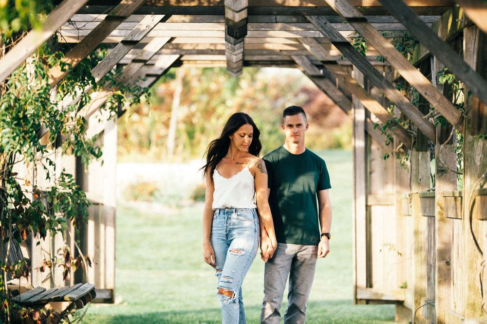 A couple walks together through a rustic wooden arbor walkway surrounded by greenery.