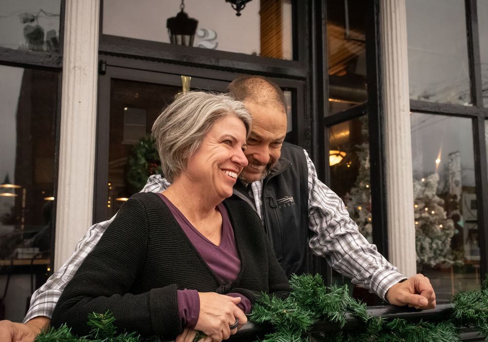People lean on a railing outside a storefront with a lantern and greenery visible in the scene.
