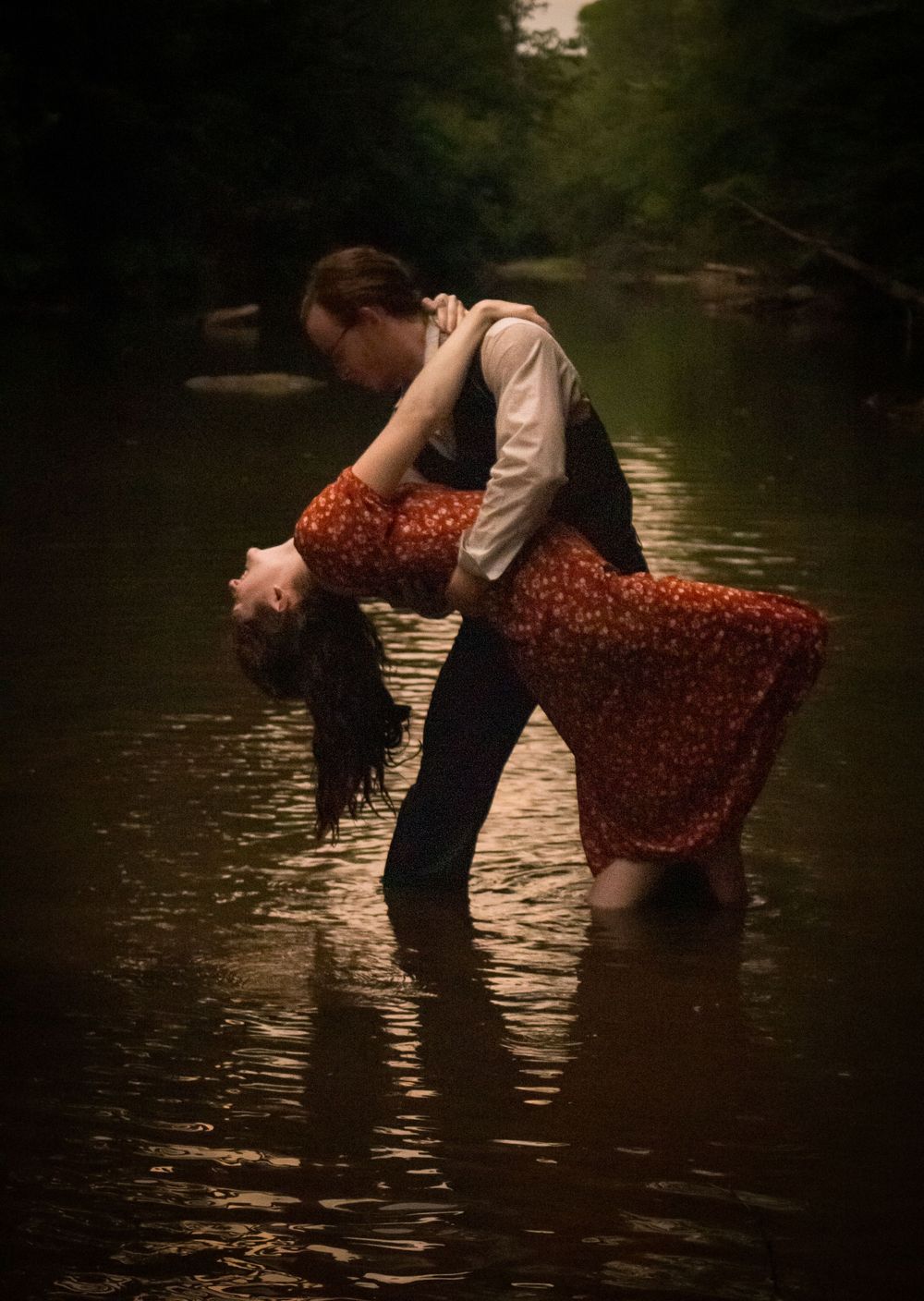 A romantic dance scene in shallow river waters with two figures creating a dramatic dip pose at dusk.