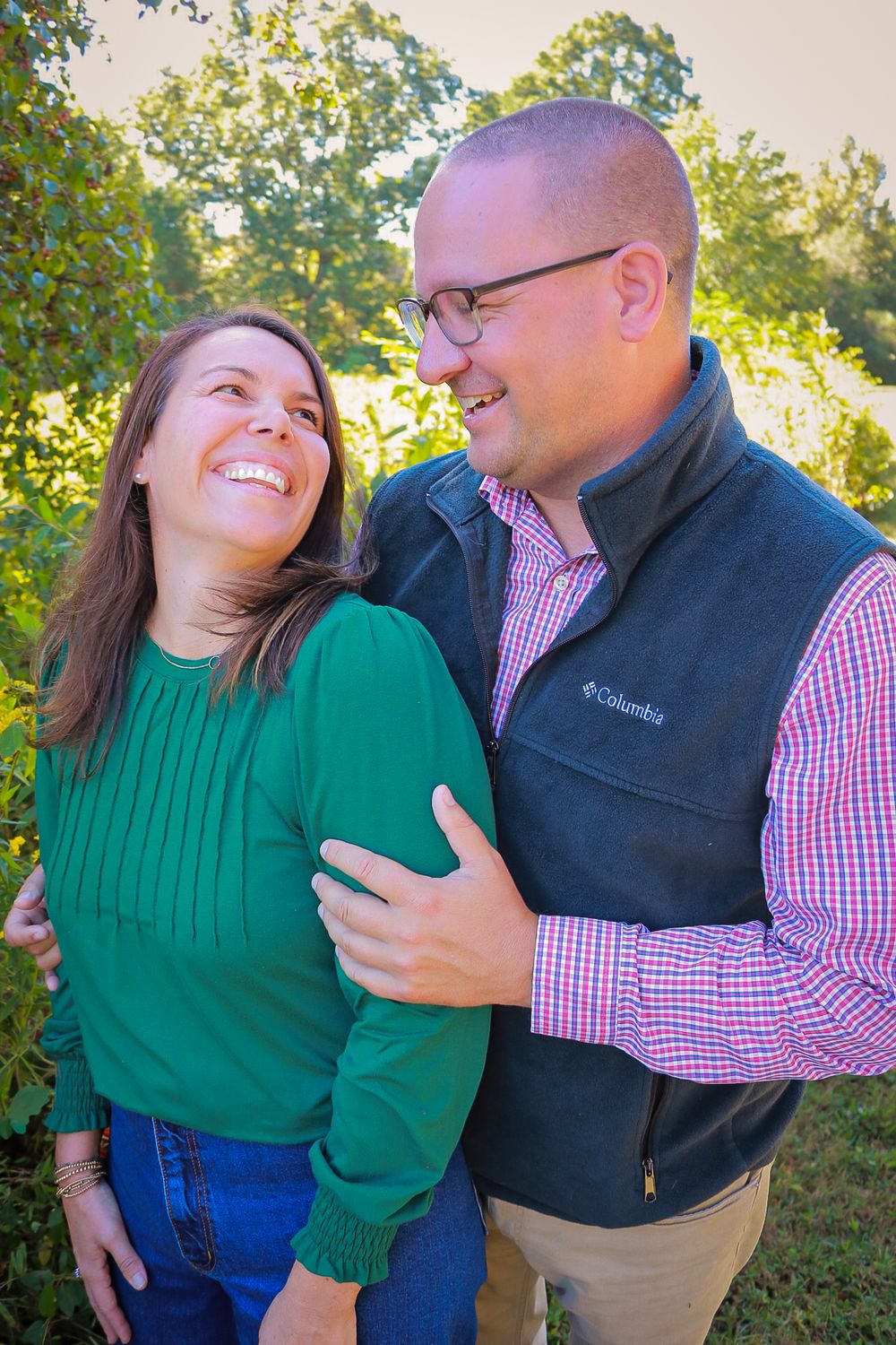 A couple in a green sweater and plaid shirt share playful candid moments outdoors during a fall photo session.