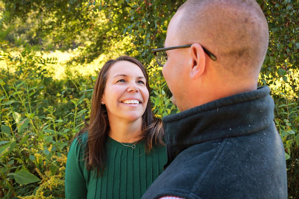A couple shares a joyful moment together outdoors surrounded by lush green foliage on a sunny day.
