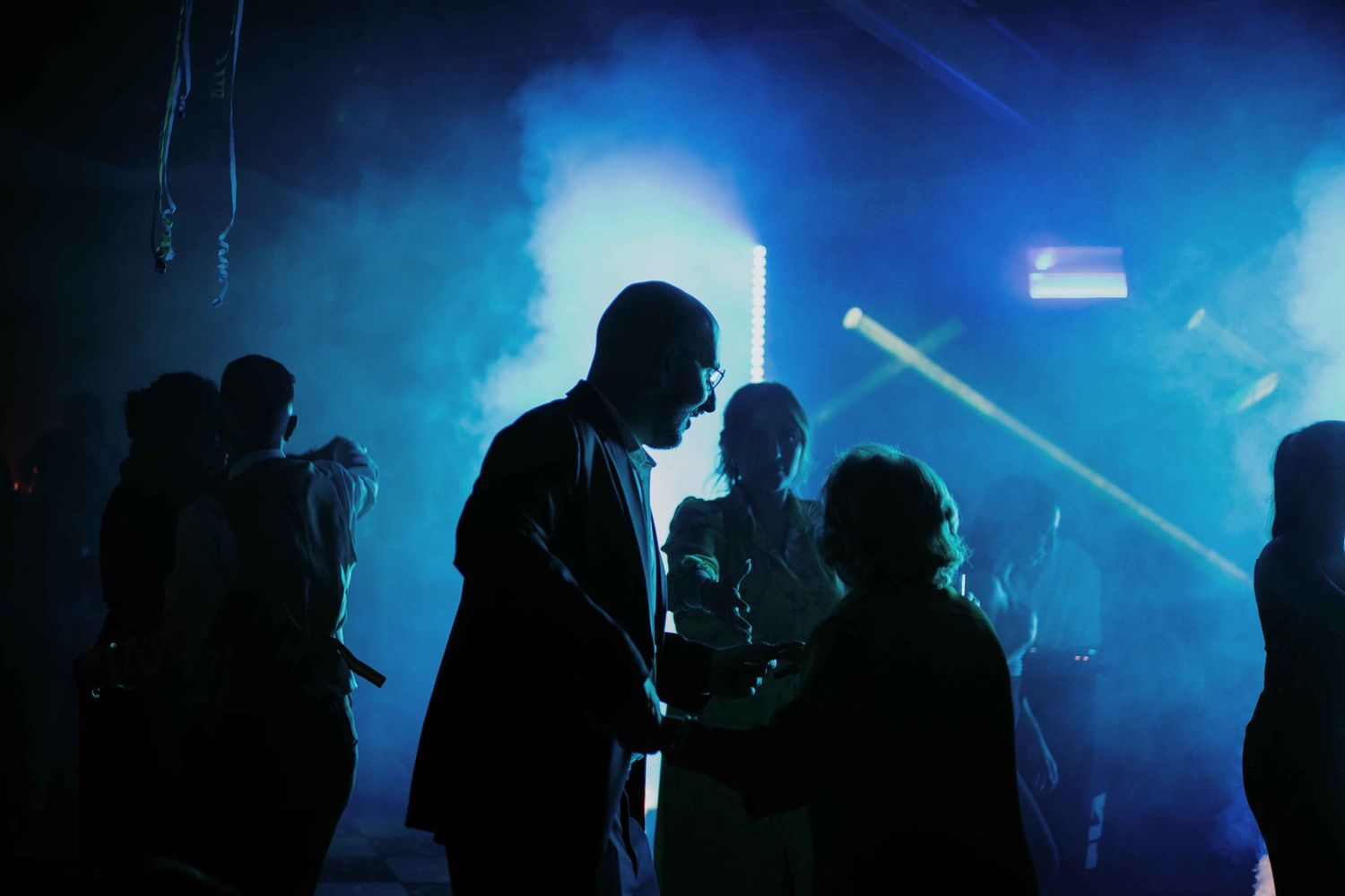 Silhouettes of people dancing in a nightclub with blue atmospheric lighting and fog effects.