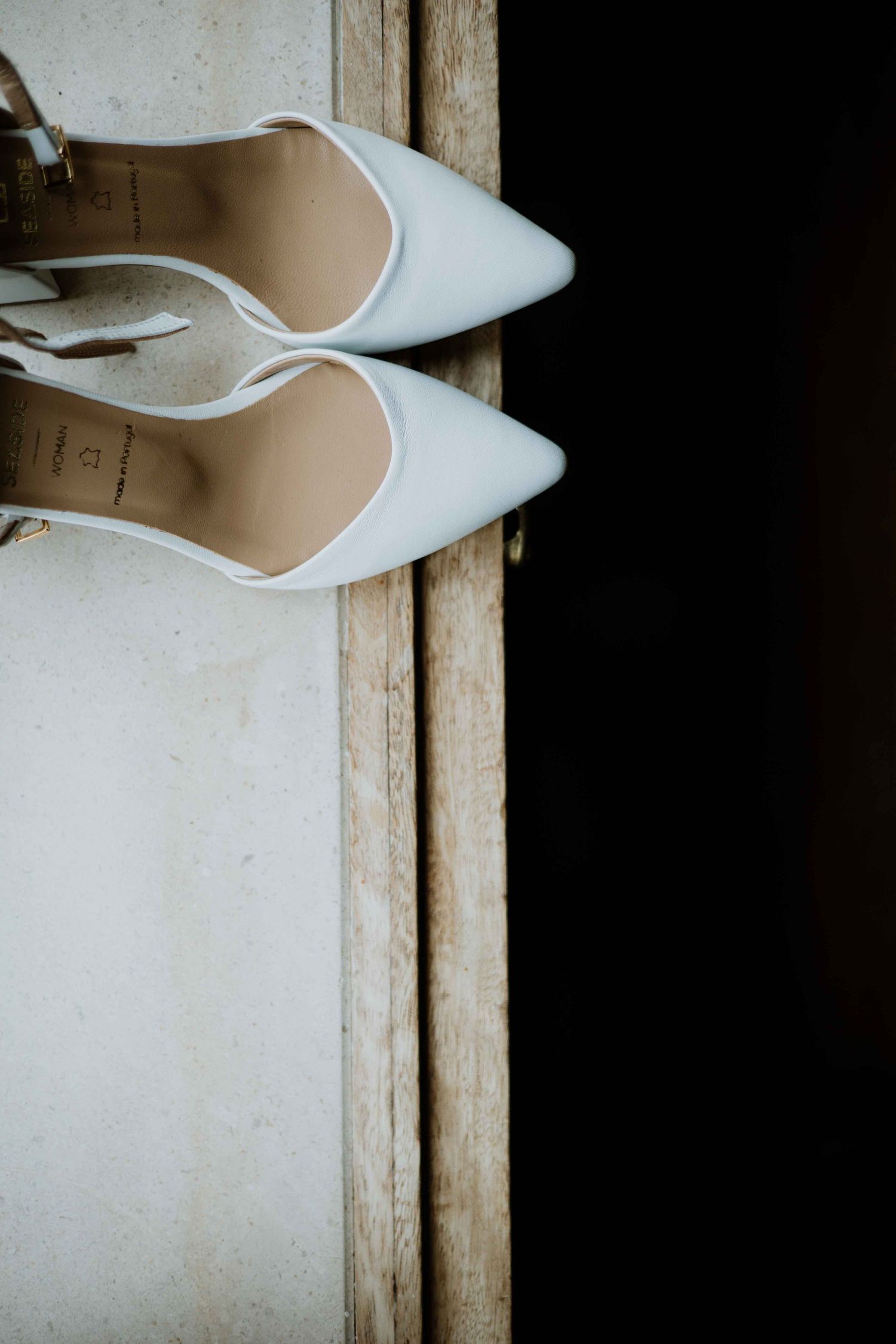 White bridal shoes rest against a rustic wooden surface with vintage texture.