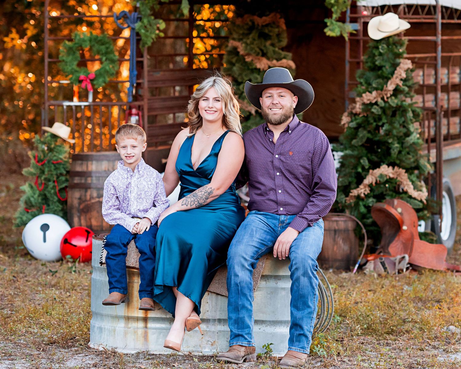 Family portrait with parents and child sitting on rustic steps with holiday decorations.