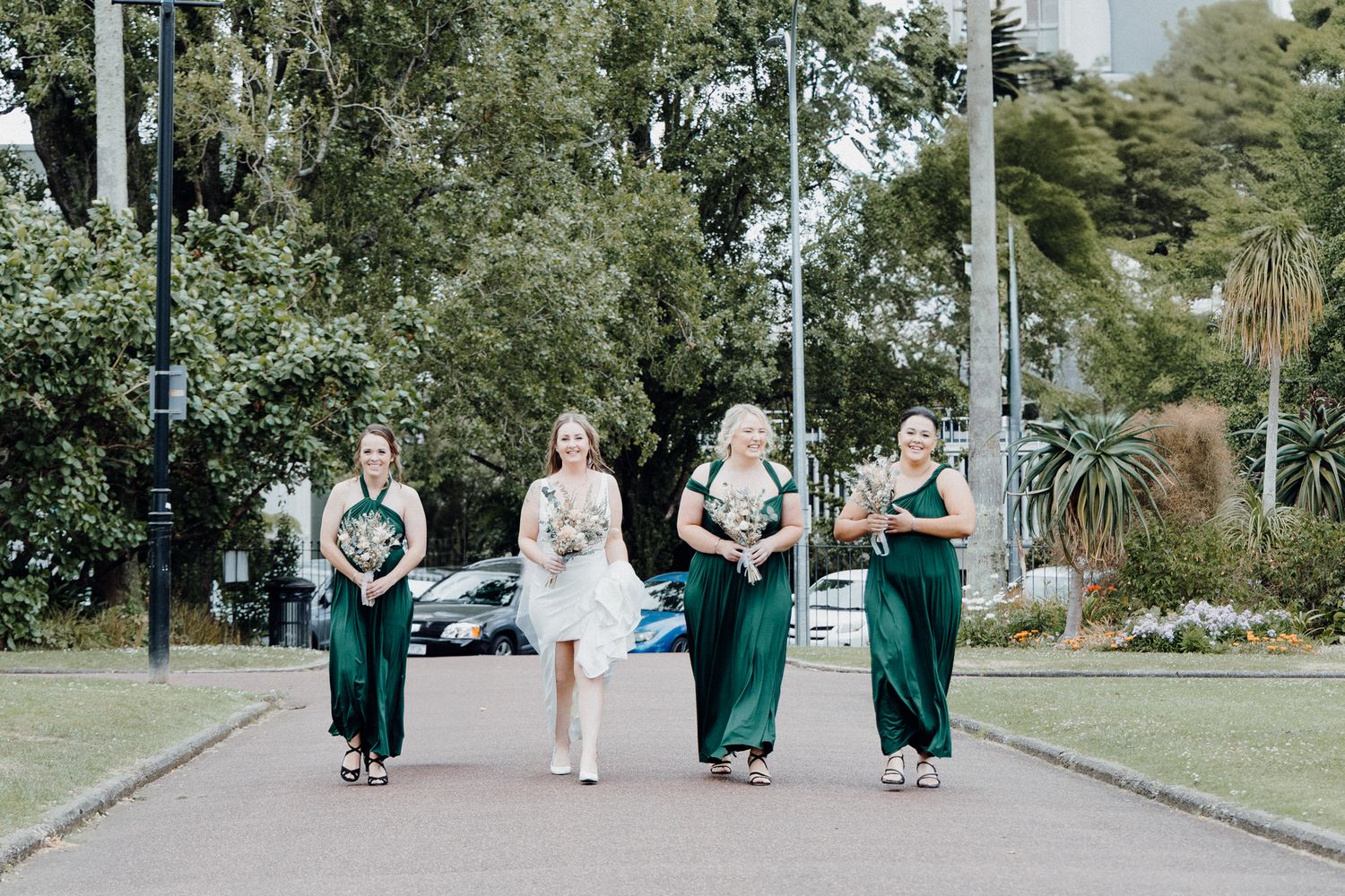 The bride and her girls walk along the pathway, captured by Apertured Media Auckland Wedding Photographer.
