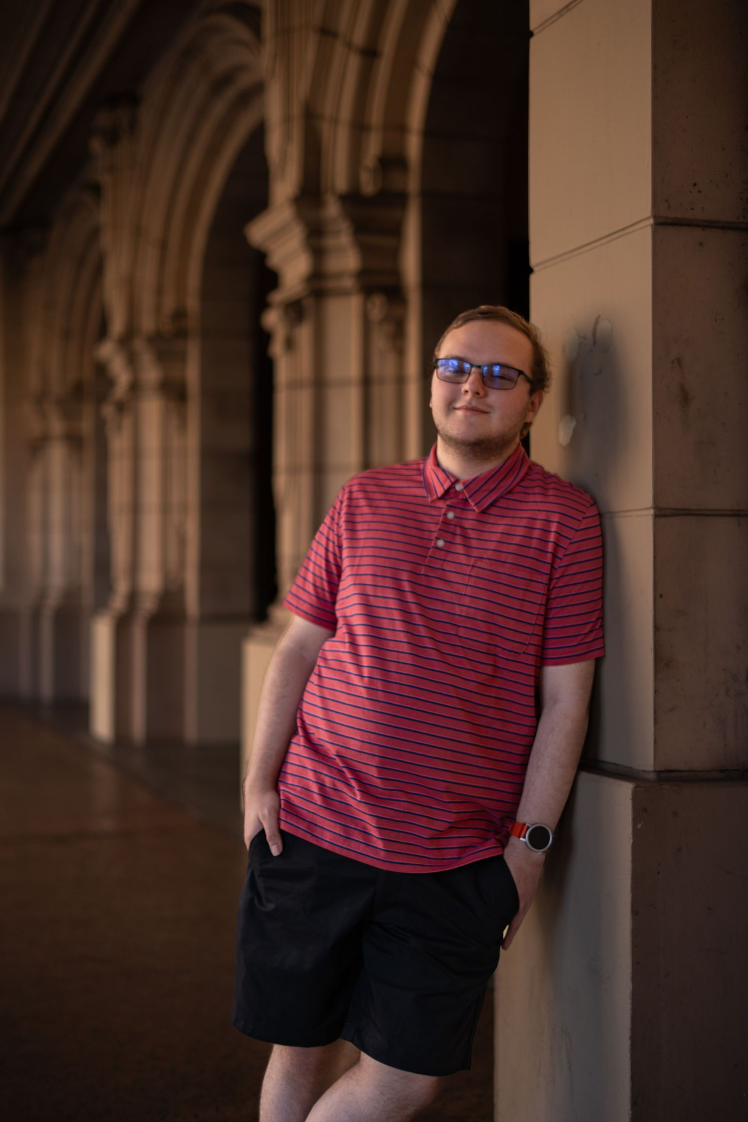Person in striped red polo shirt poses against architectural columns in dramatic lighting.