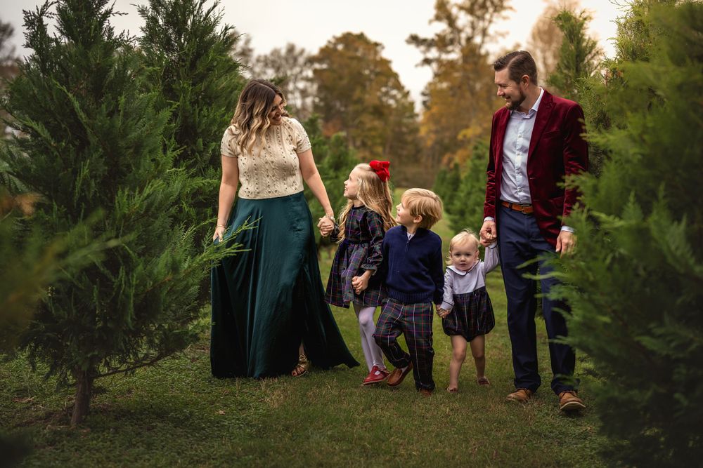 Family wearing coordinated outfits walking together among evergreen trees at sunset in a Christmas tree farm setting.
