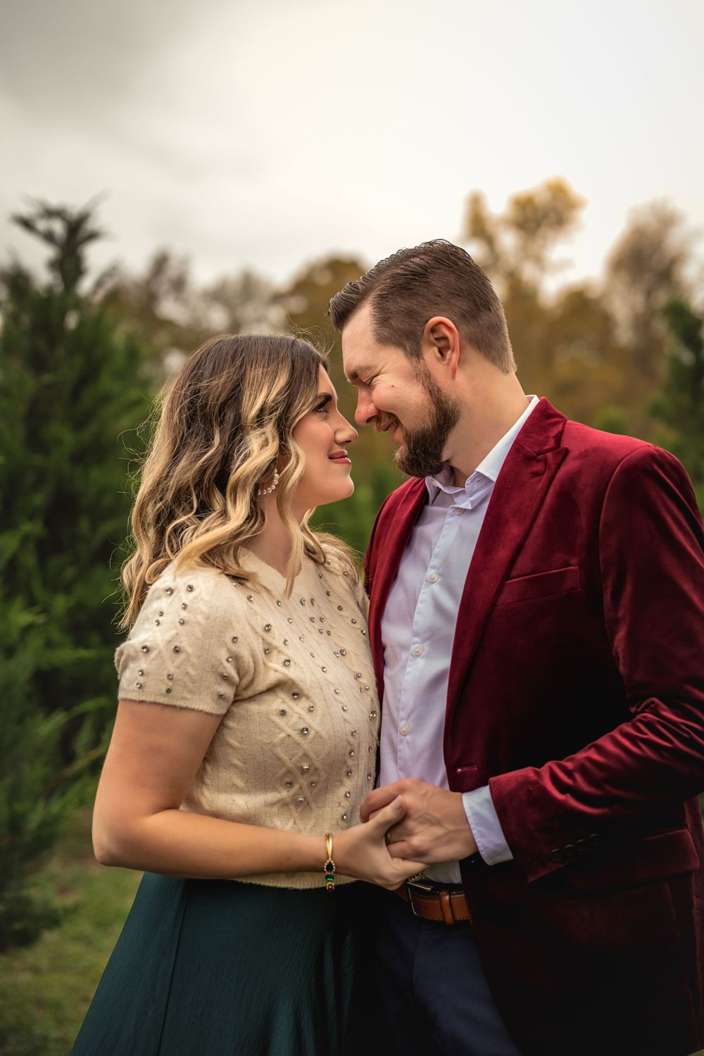 A romantic moment at a Christmas tree farm with burgundy velvet and cream colored attire.