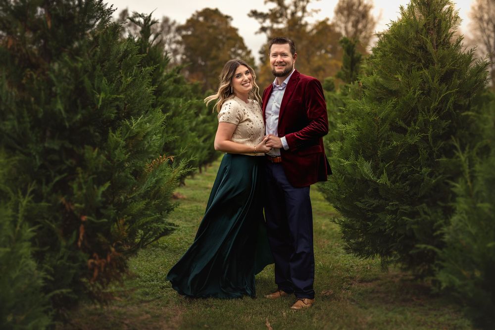 A couple embraces during a romantic photoshoot between evergreen trees at a Christmas tree farm.