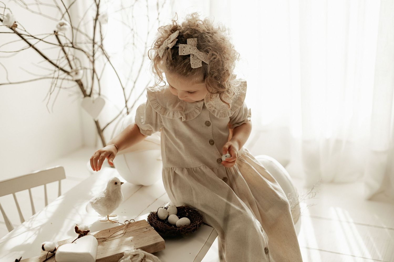 A dreamy sepia-toned photo showing a child in ruffled clothing amidst delicate decor and branches.