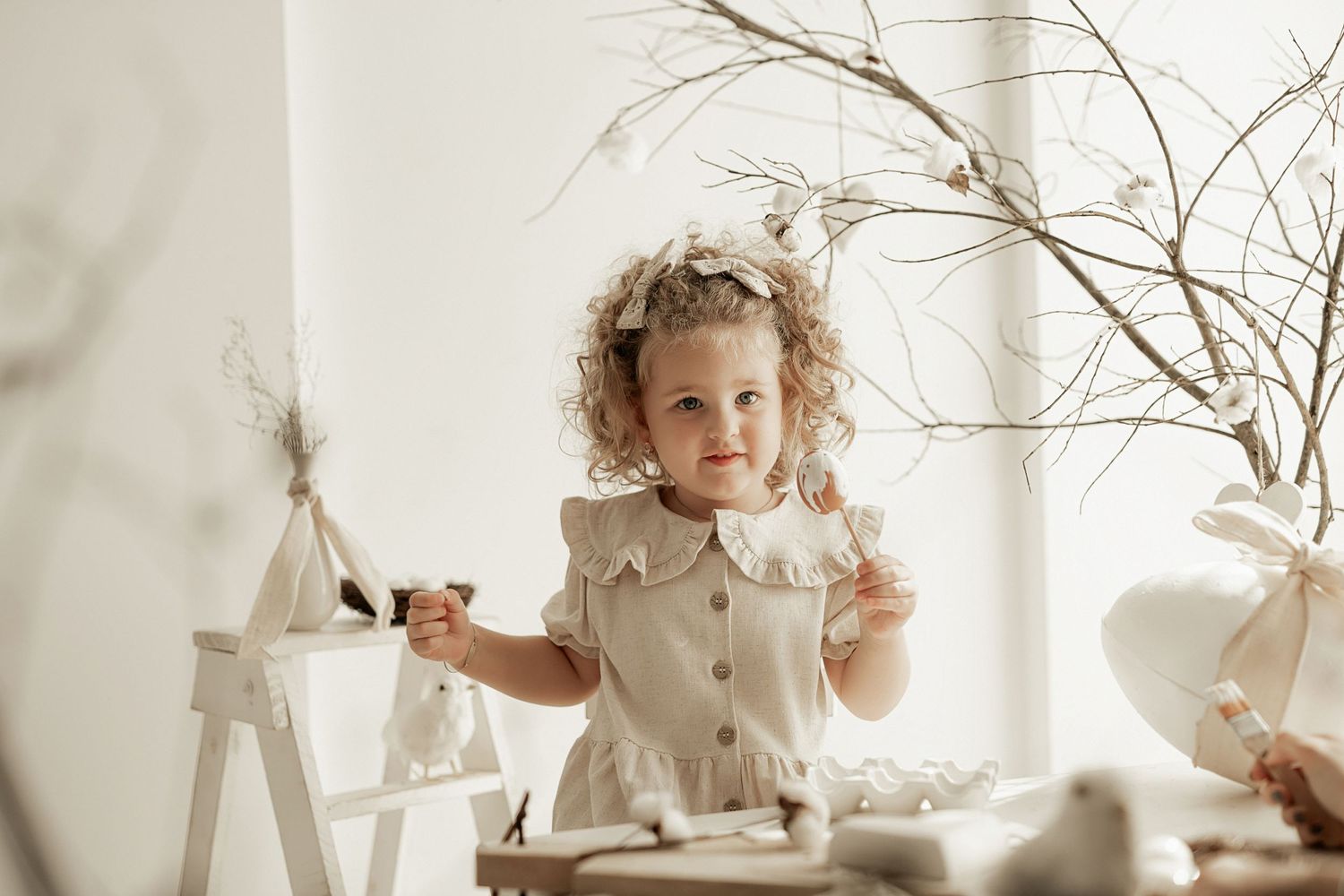 A light-filled artistic photo capturing a child playing at a decorated table with bare branches and white accents.
