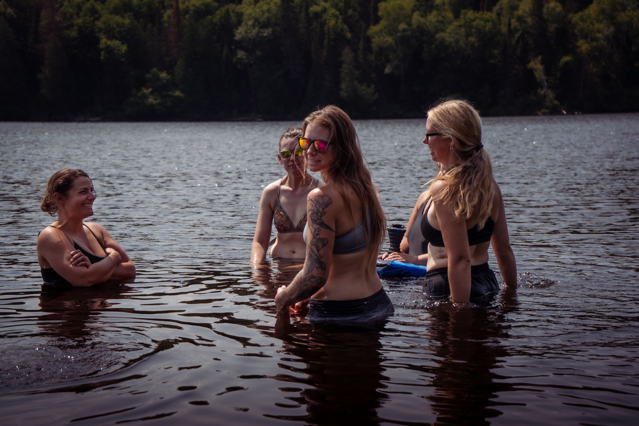 Four people enjoying a summer swim in a serene lake surrounded by forest on a warm day.