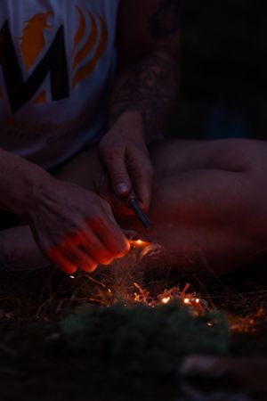 Hands using flint and steel to ignite tinder for starting a campfire in dim evening light.