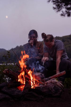 A cozy campfire glows in the twilight as campers gather around smoke and flames on a peaceful evening outdoors.