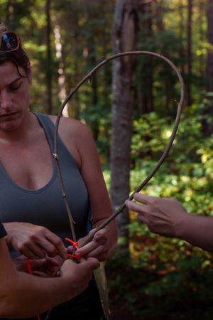Two hands work together to manipulate red-handled gardening shears while pruning branches in a sunlit forest.
