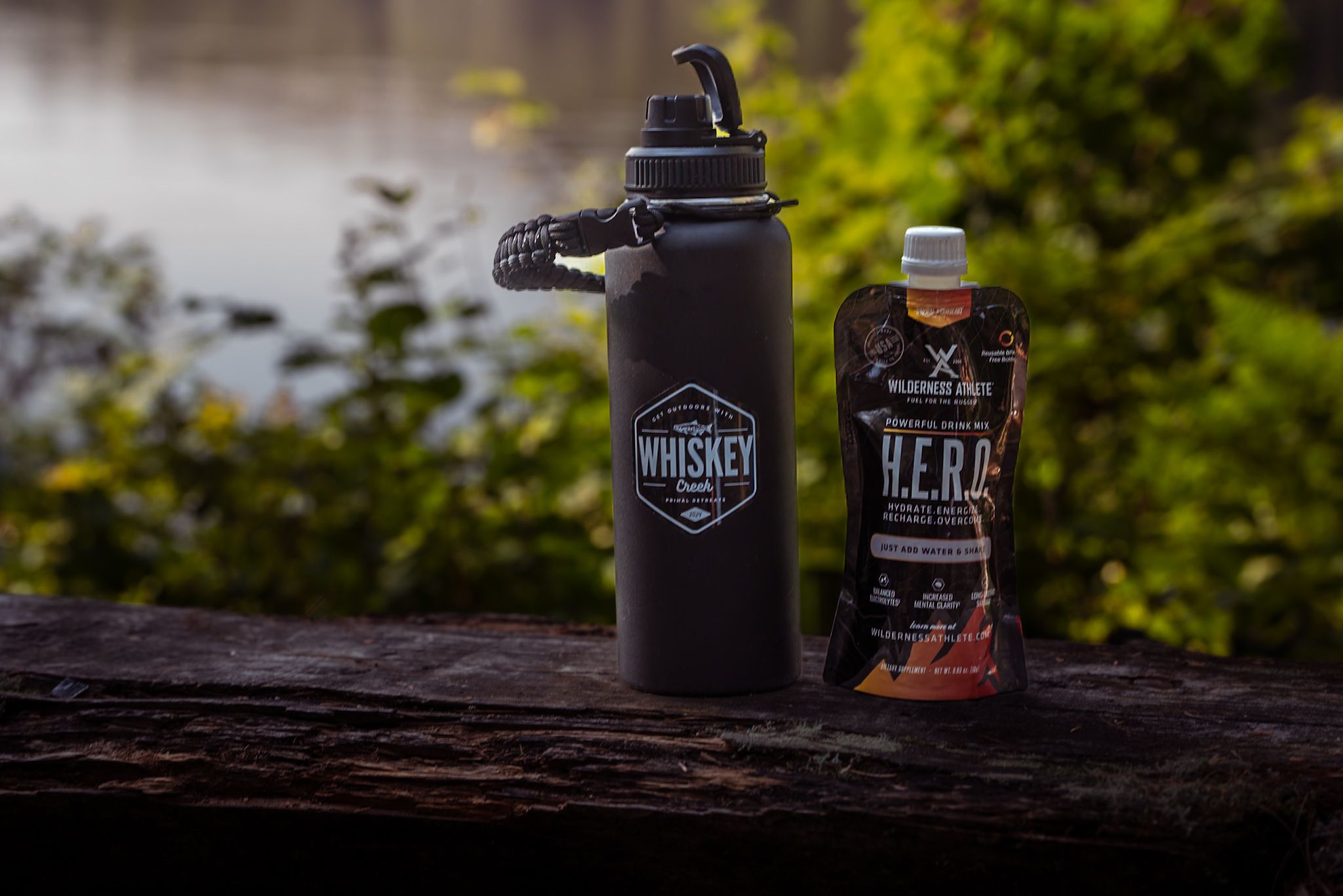 A black water bottle and energy drink sit on a wooden surface against a blurred natural background.
