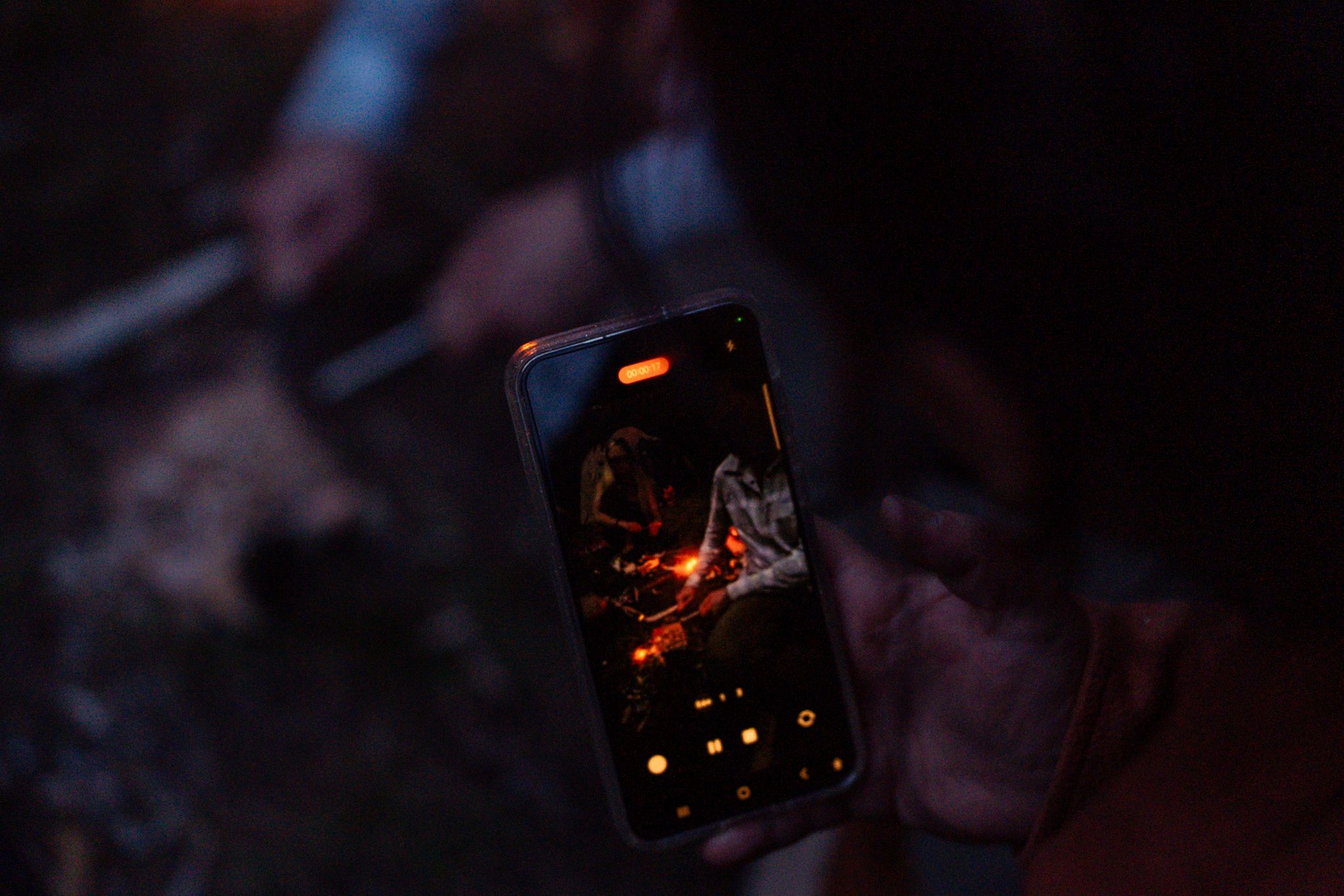 Smartphone screen displays glowing campfire embers in dark nighttime setting.