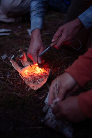 Someone uses a fire starter tool to ignite tinder and kindling for starting a campfire in the dark.