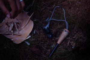 Garden tools and worn leather work gloves lying on dark soil and mulch in low light conditions.