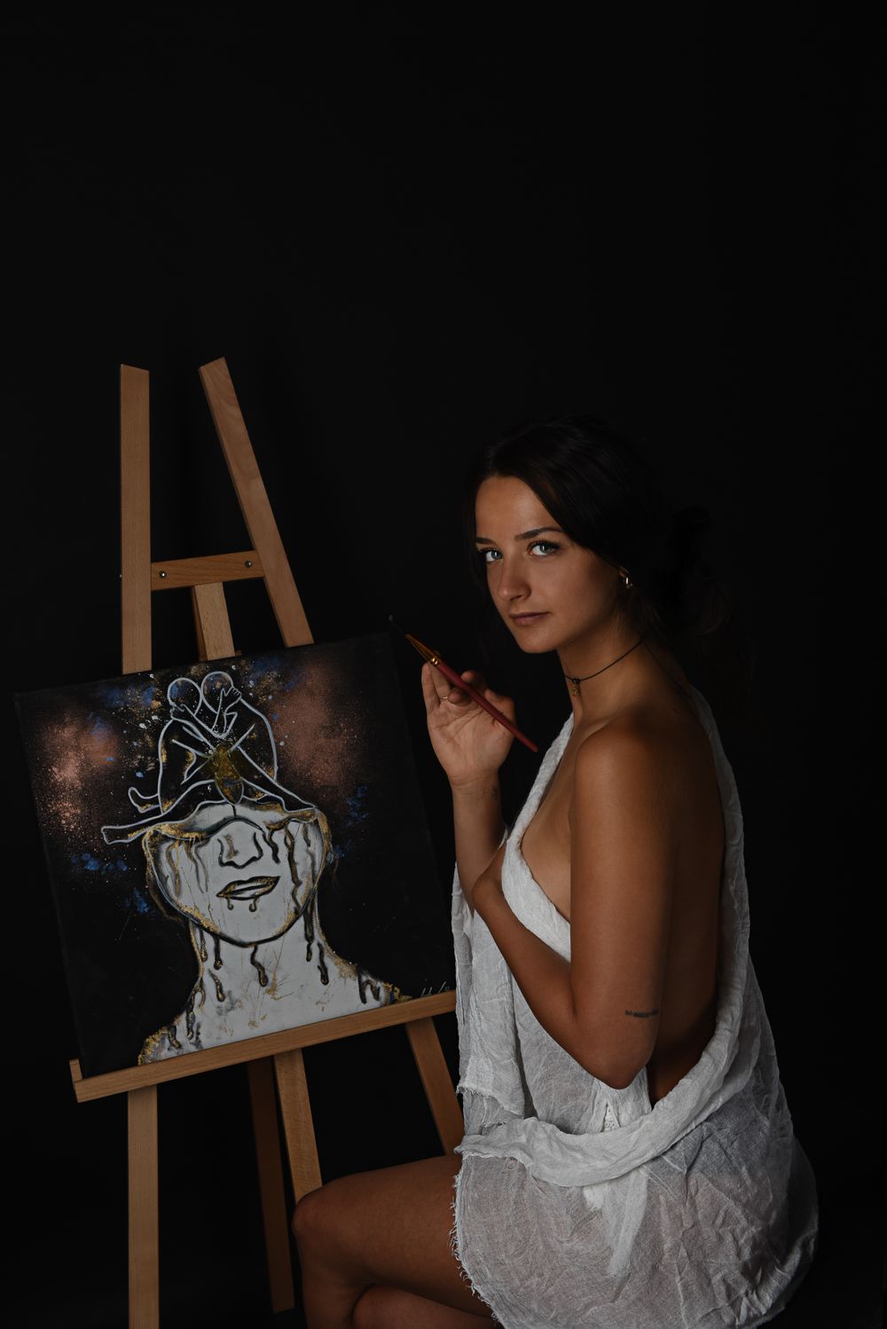 Fine Art Fotografie. Artist posing next to an easel with ethereal artwork in a dimly lit studio setting.
