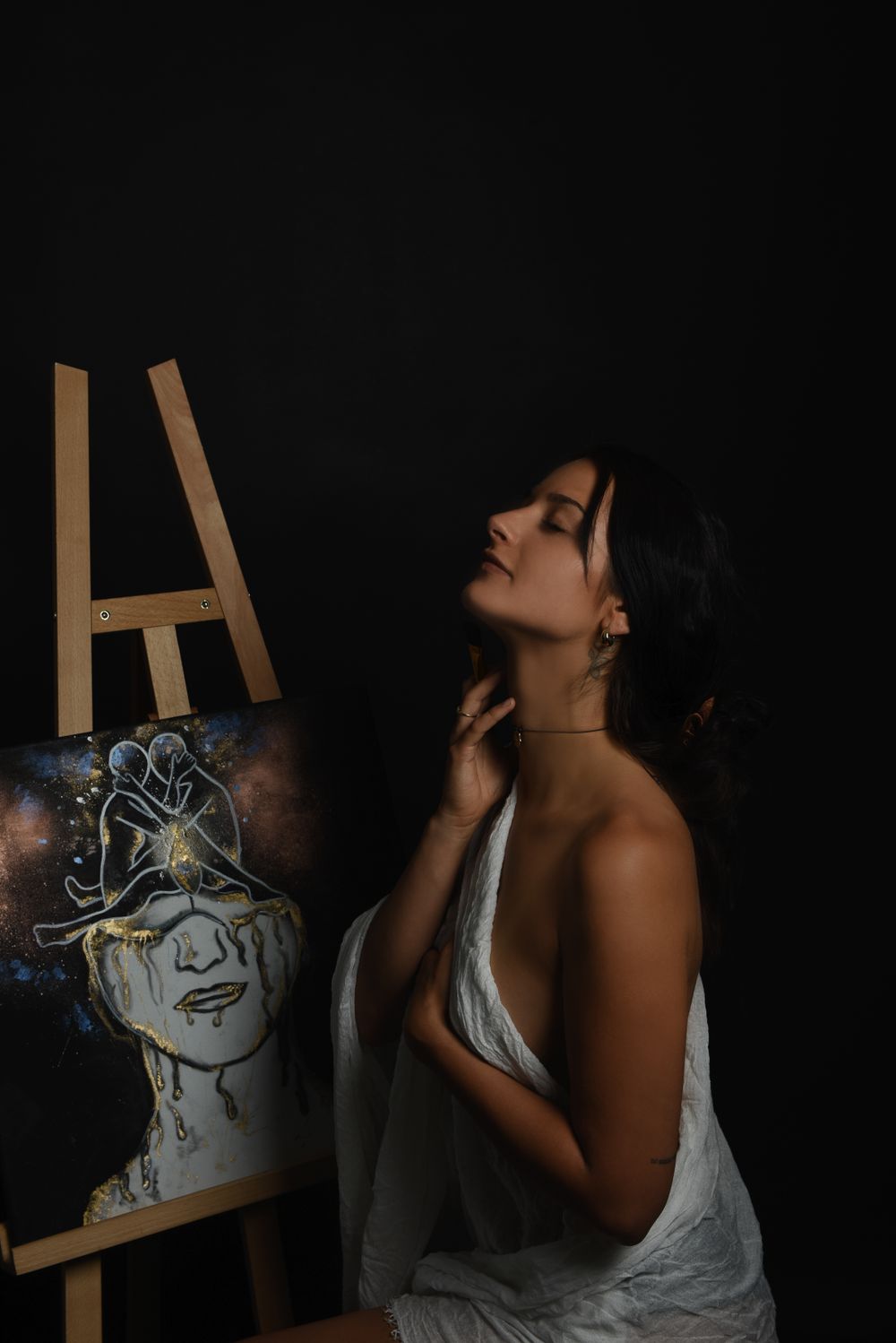 Fine Art Portrait. Artistic boudoir portrait with ethereal painting on easel in moody lighting.