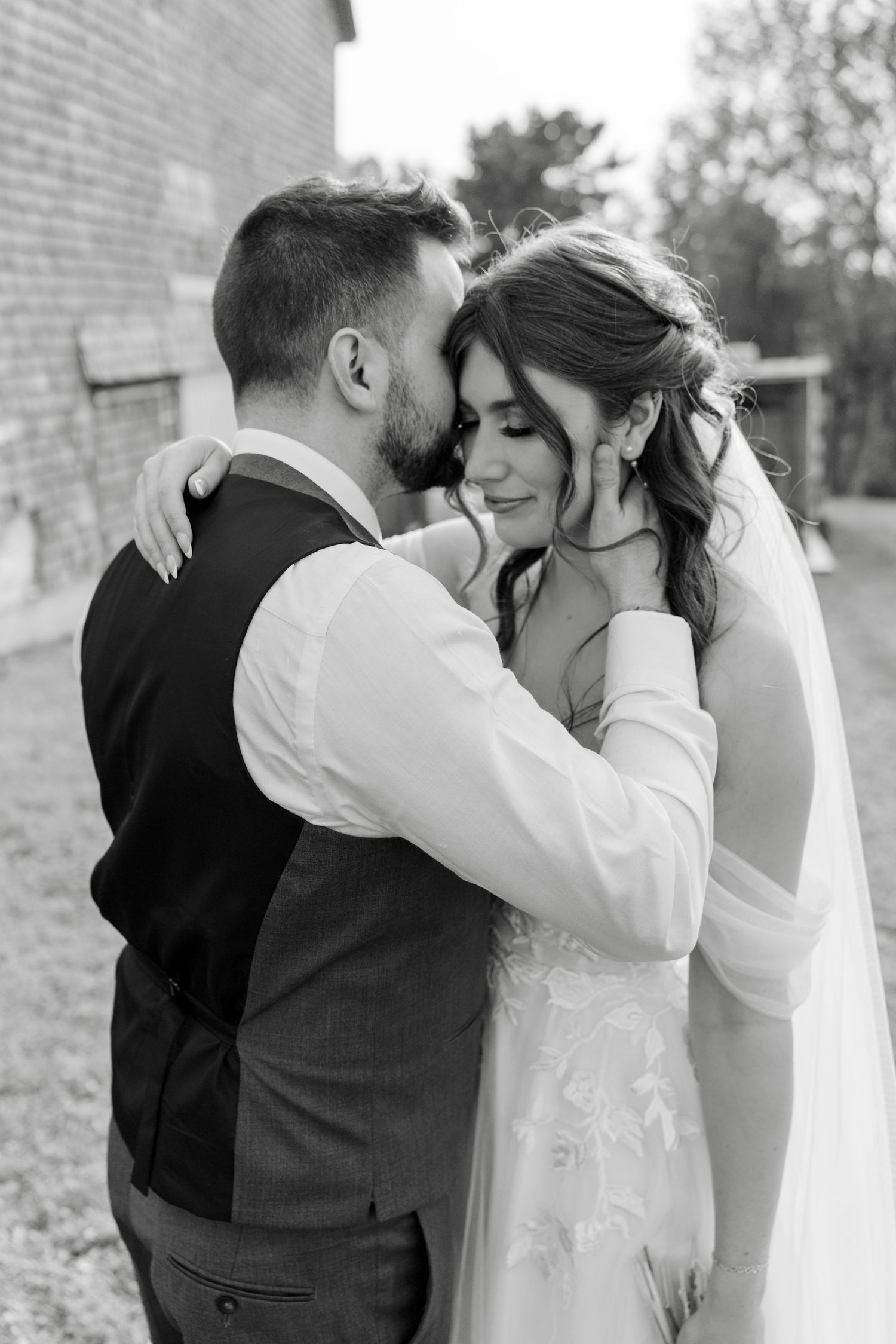 Black and white portrait of bride and groom sharing an intimate moment, groom whispering to bride at Nova Scotia barn wedding.