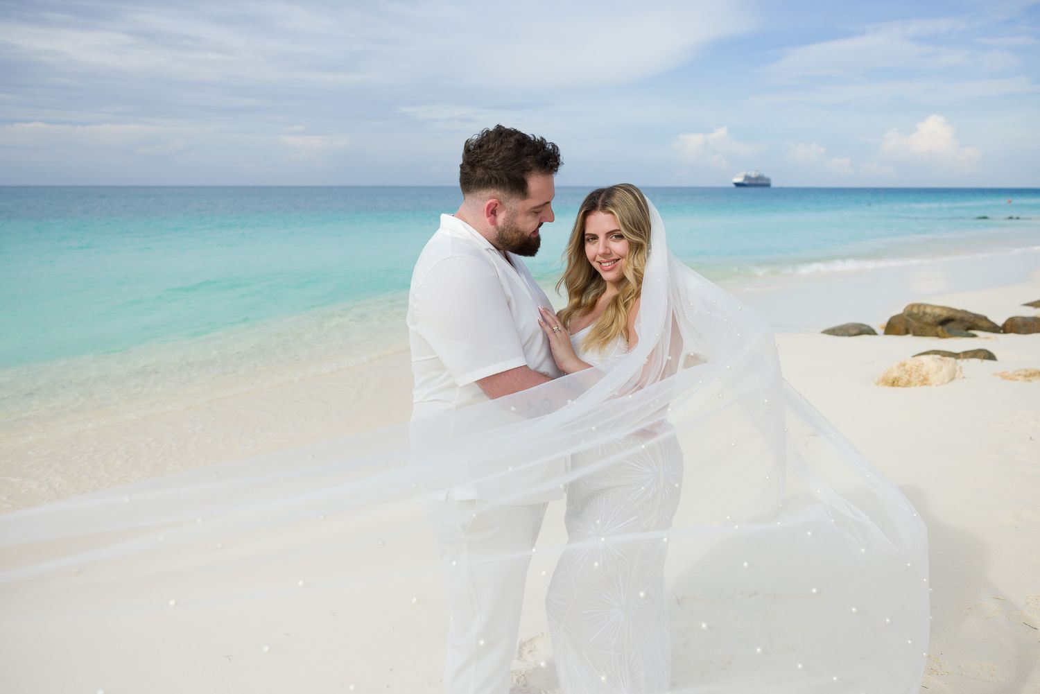 Couple walking hand in hand along pristine white sand beach with turquoise ocean waters in the background.