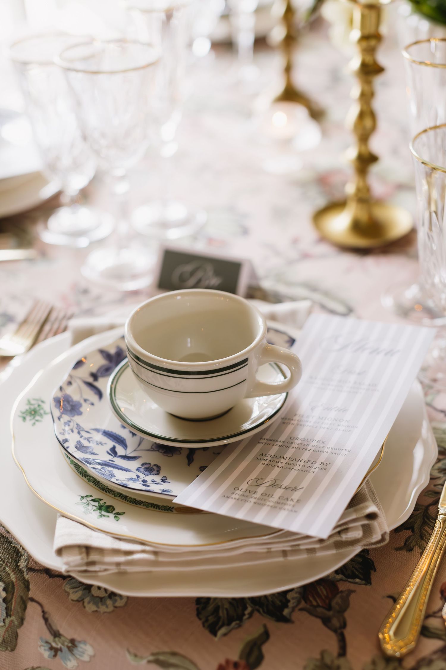 An elegant place setting with vintage teacup, floral plates, and brass candlestick on a delicate tablecloth.