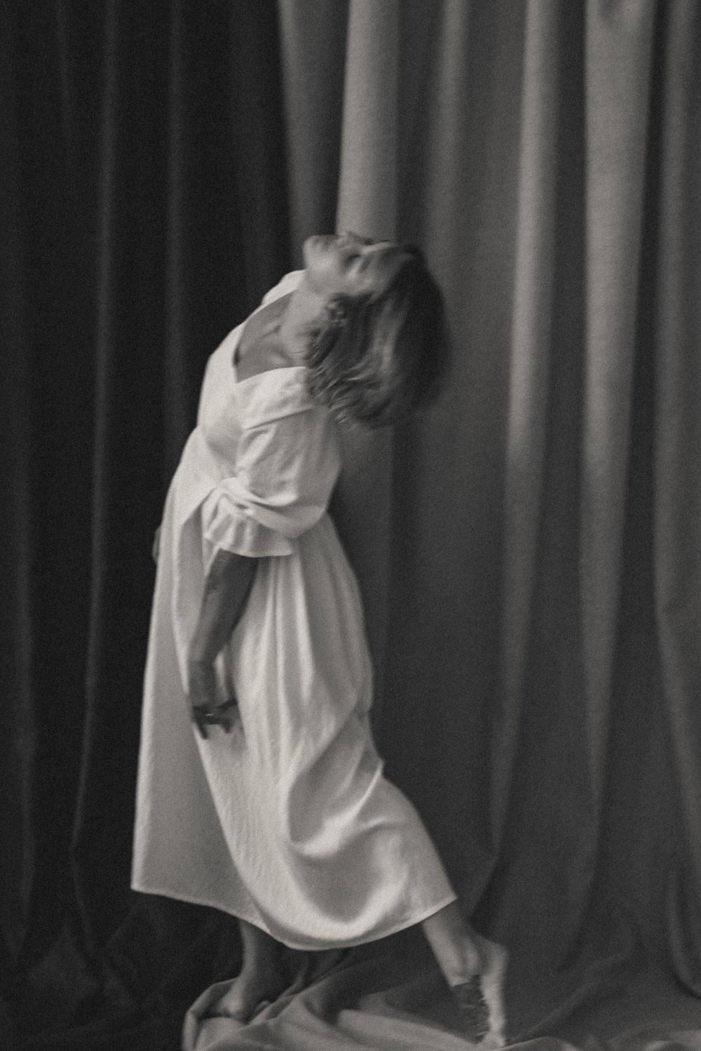 Ethereal dance sequence in white dress against dark curtained backdrop.