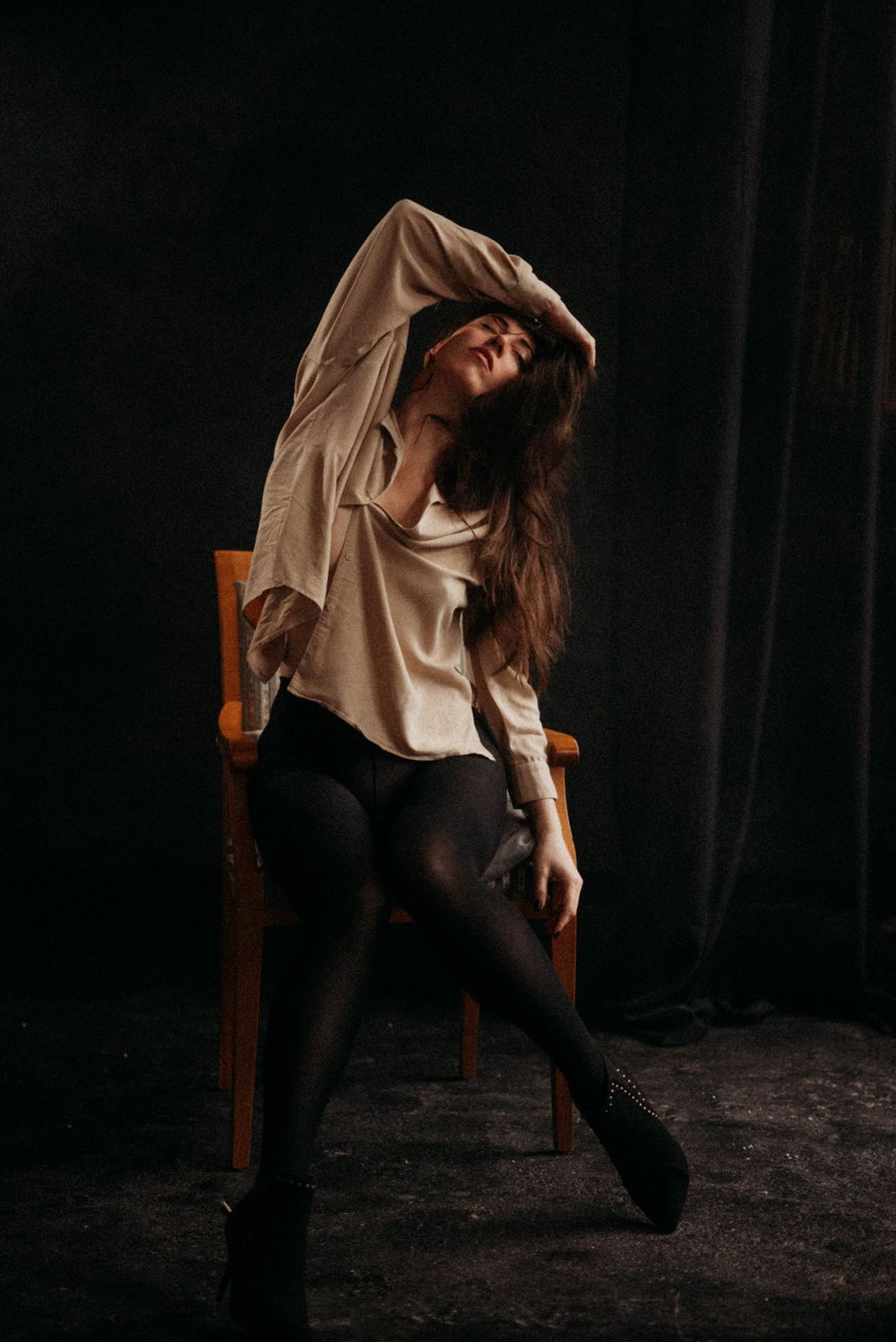 Dramatic dance pose on wooden chair against dark background with flowing movement.