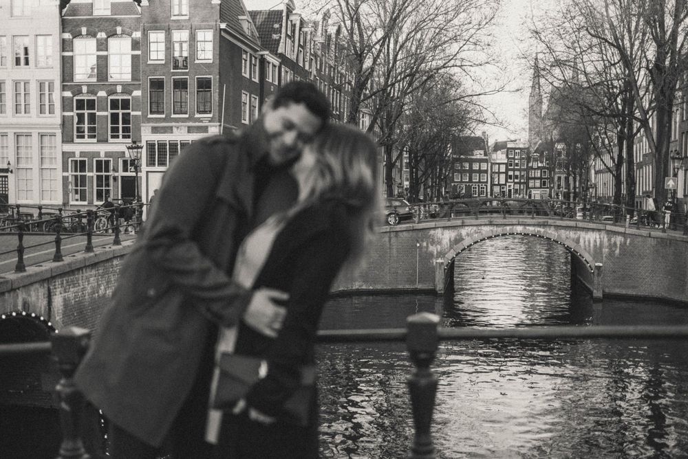 Couple embracing romantically on an Amsterdam canal bridge in black and white photography.
