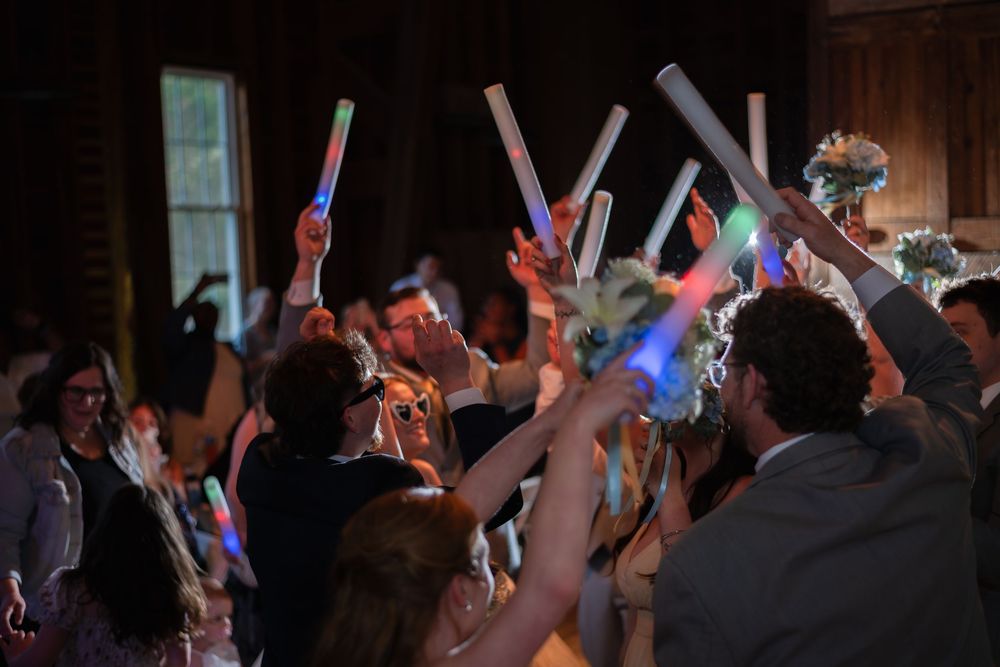 Wedding guests celebrating with colorful LED glow sticks raised in the air during a festive indoor reception.