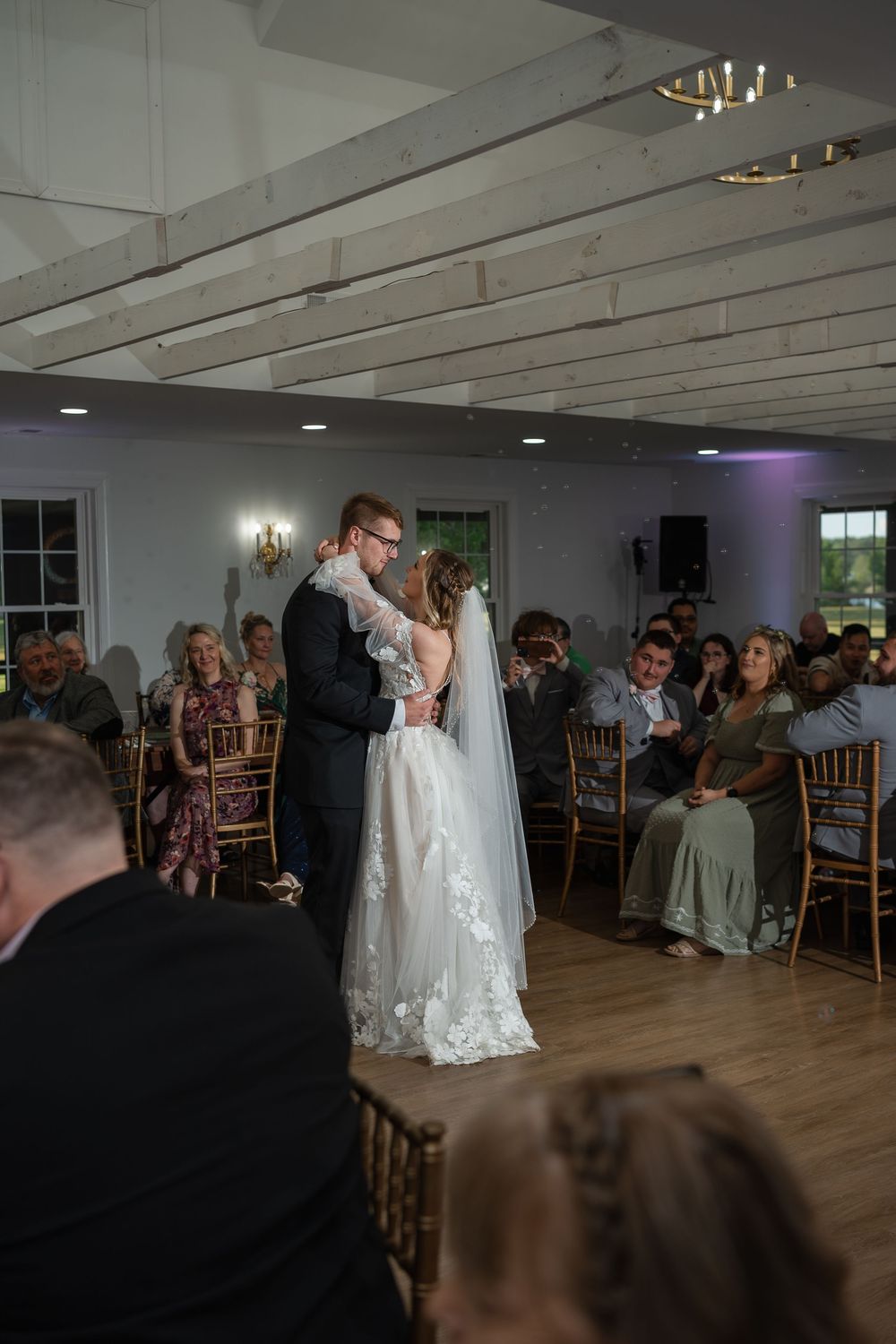 Bride and groom share their first dance at an elegant indoor wedding reception with guests seated around them.
