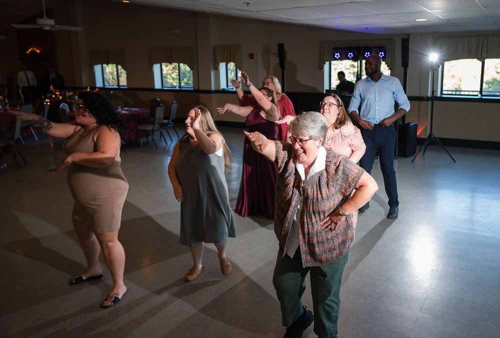 People dancing together at a wedding venue with wooden floors and natural lighting.