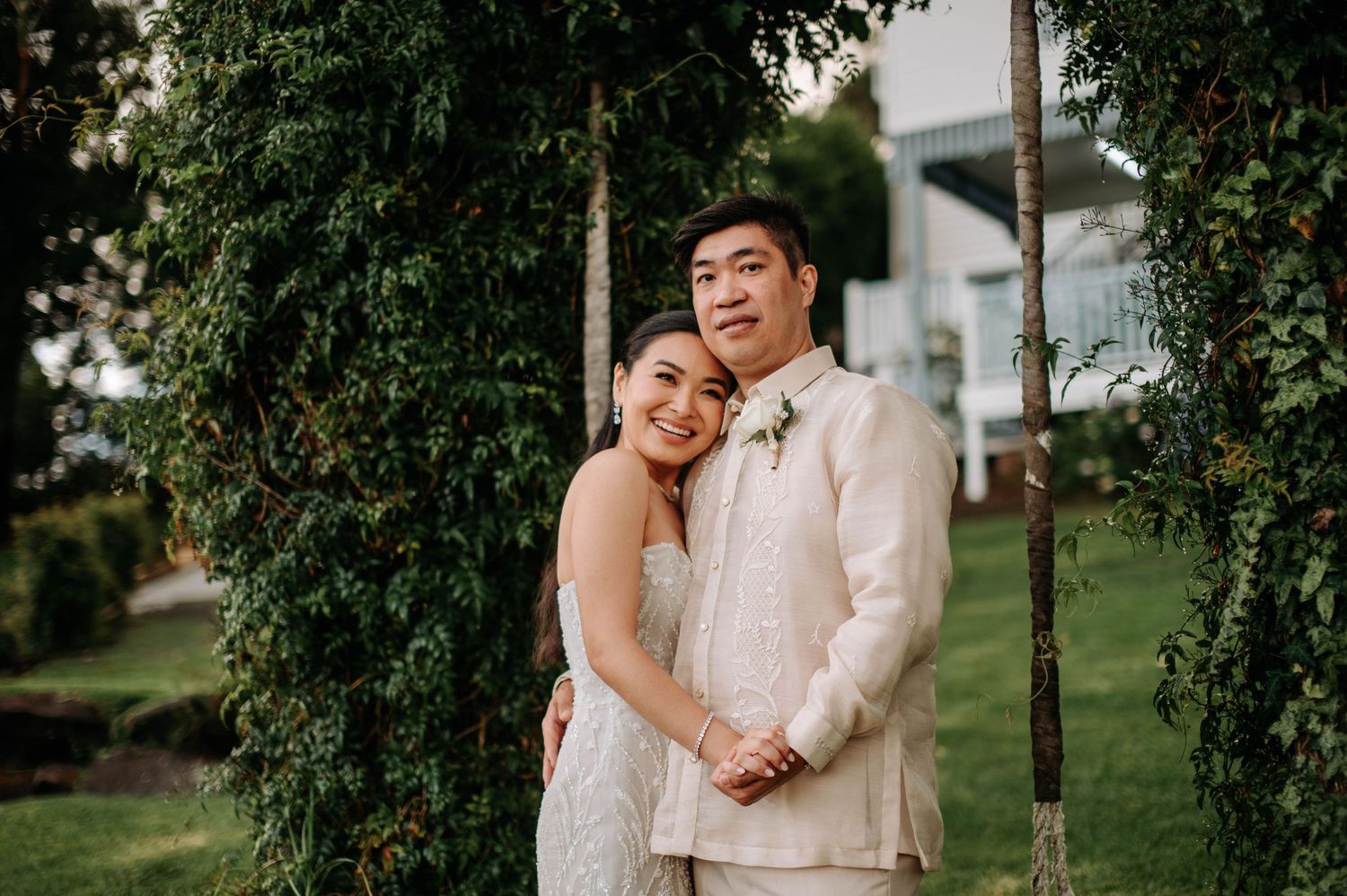 Newlyweds embrace in a garden setting surrounded by lush greenery.
