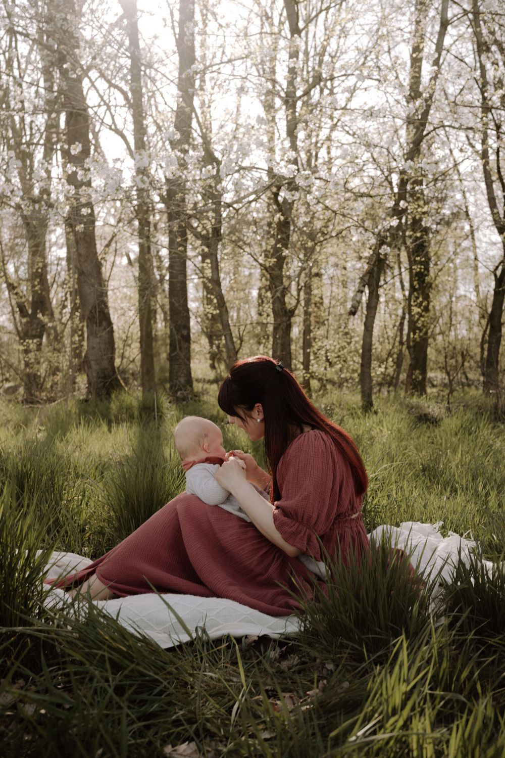 A tender moment captured in a misty forest setting with white blanket and tall trees.