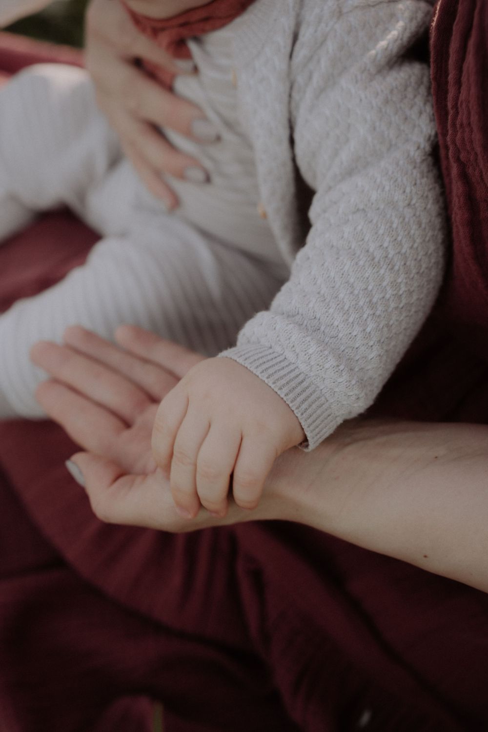 Close-up of baby's small hand holding parent's hand against burgundy fabric.