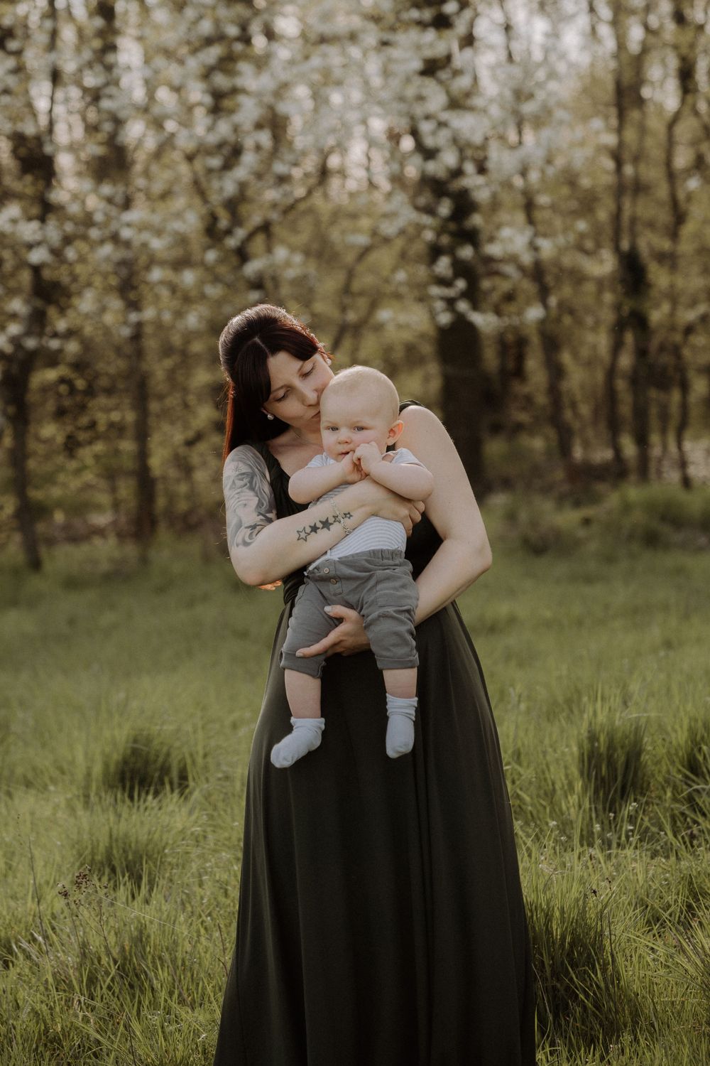 Parent and baby share tender embrace while standing in sunlit spring forest.