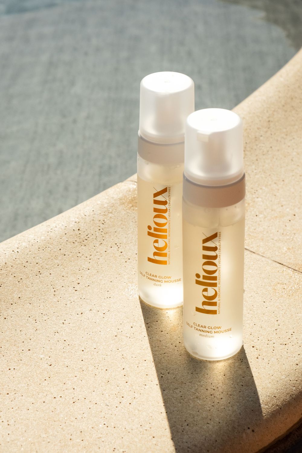 Two skincare product bottles labeled Helioux displayed on beige surface in natural lighting.