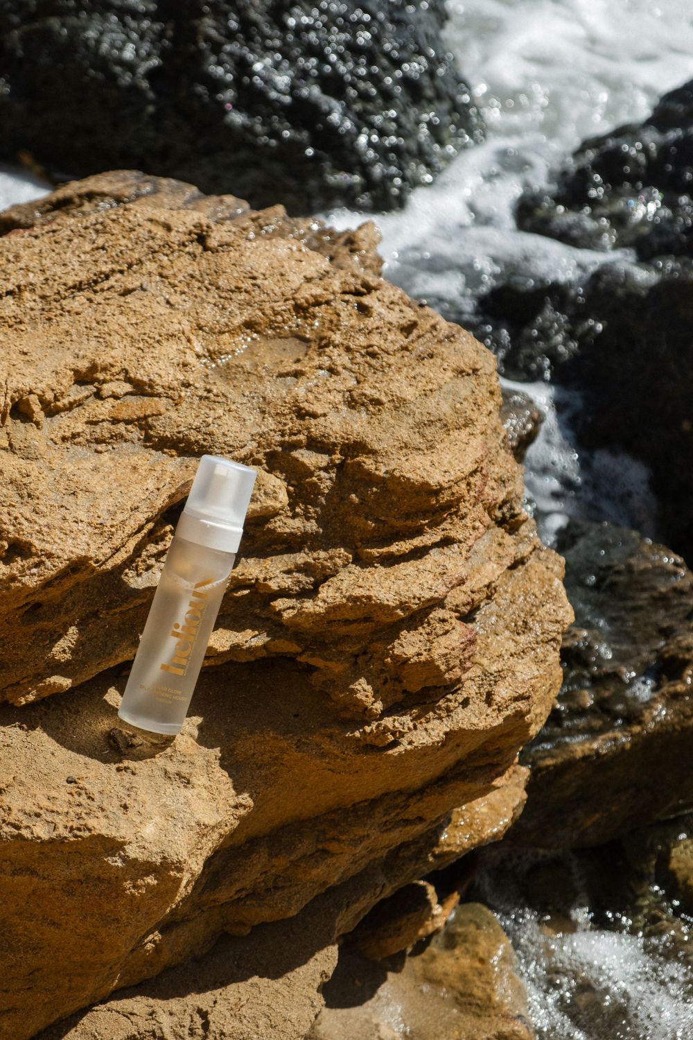 Beauty product bottle placed on rocky terrain with rushing water in background.