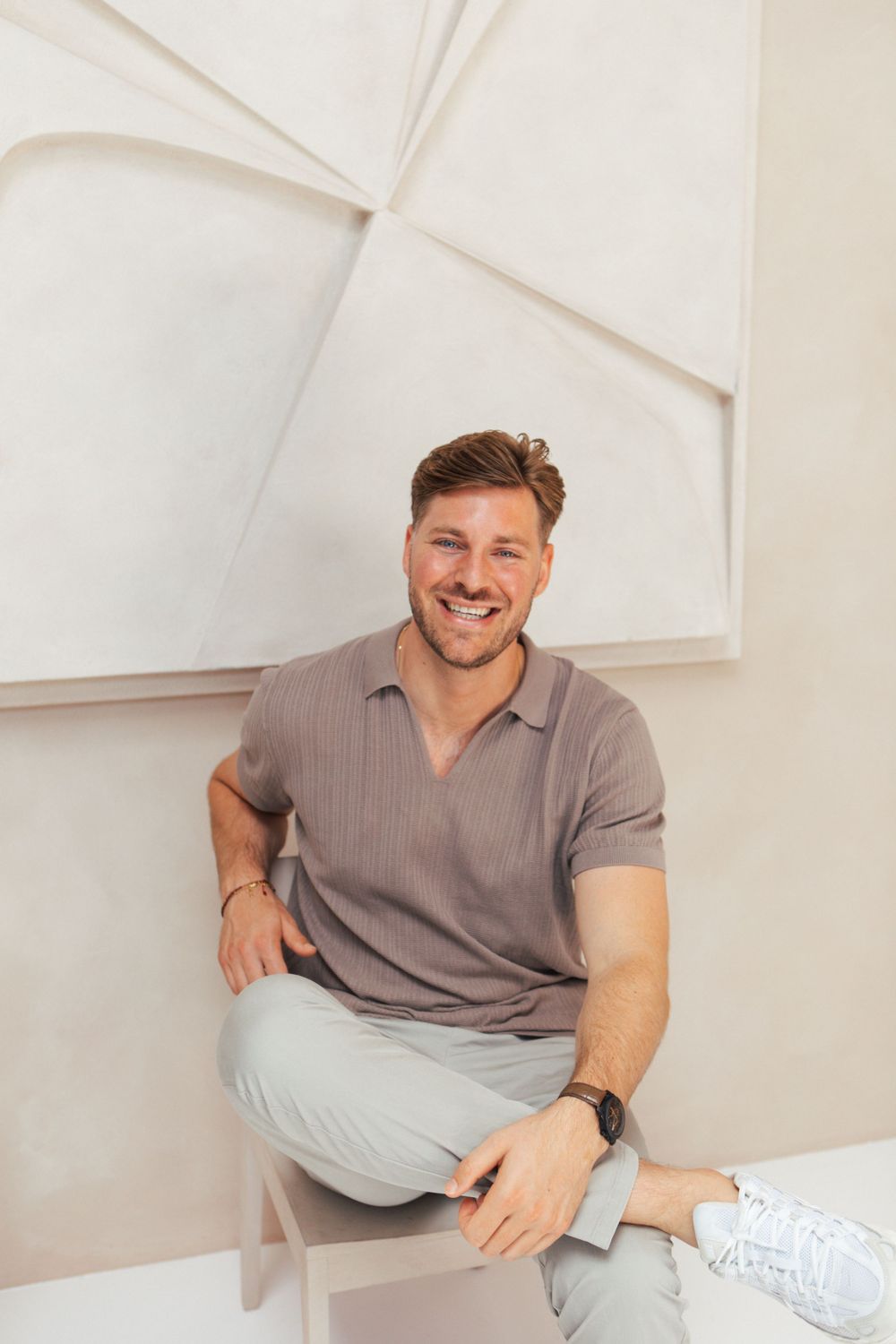 Person in casual polo shirt sitting on white bench against textured wall.