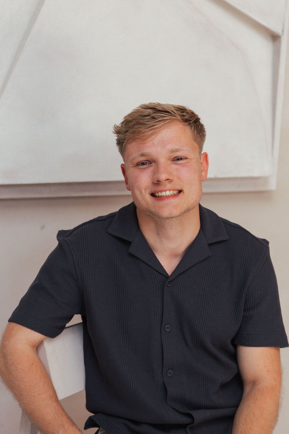 Person in navy polo shirt smiling against textured wall background.