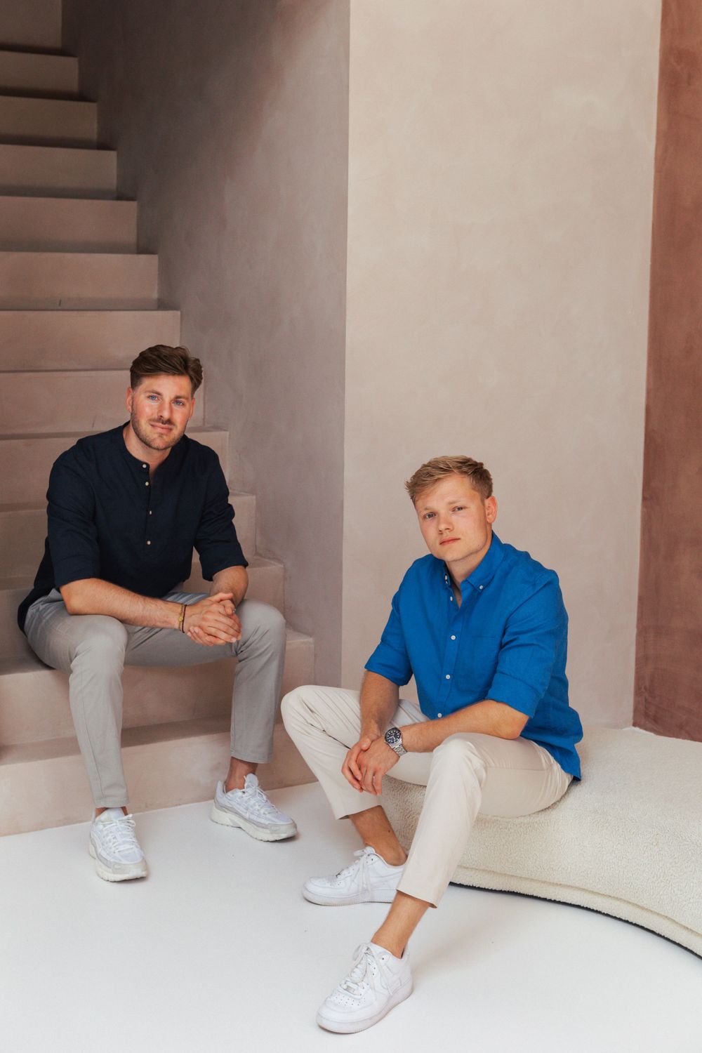 Two people sitting on modern stairs in casual business attire.