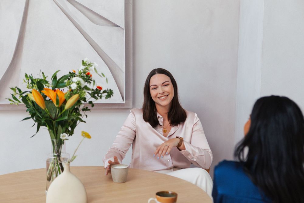 Two people having conversation at table with flowers and coffee.