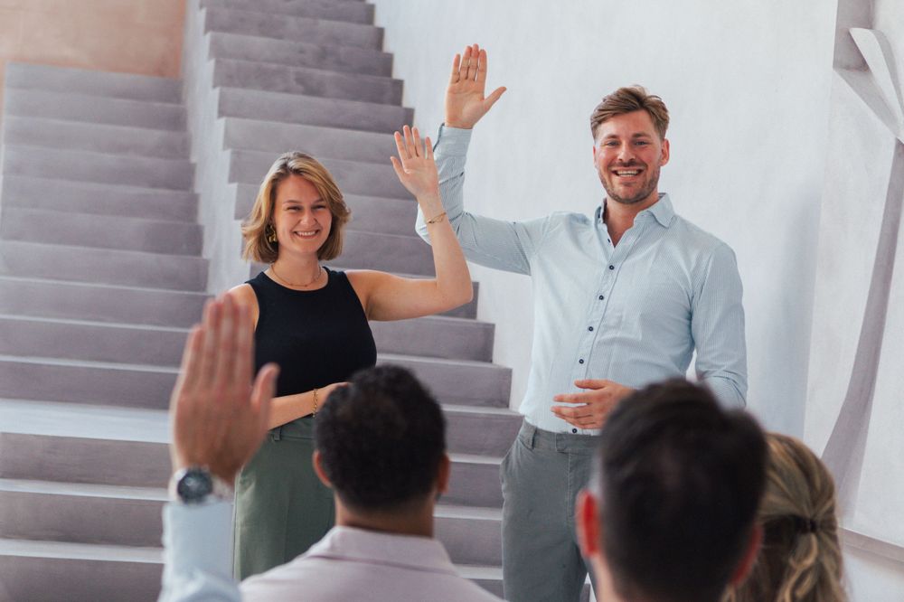 Two people raising hands in greeting during business meeting.