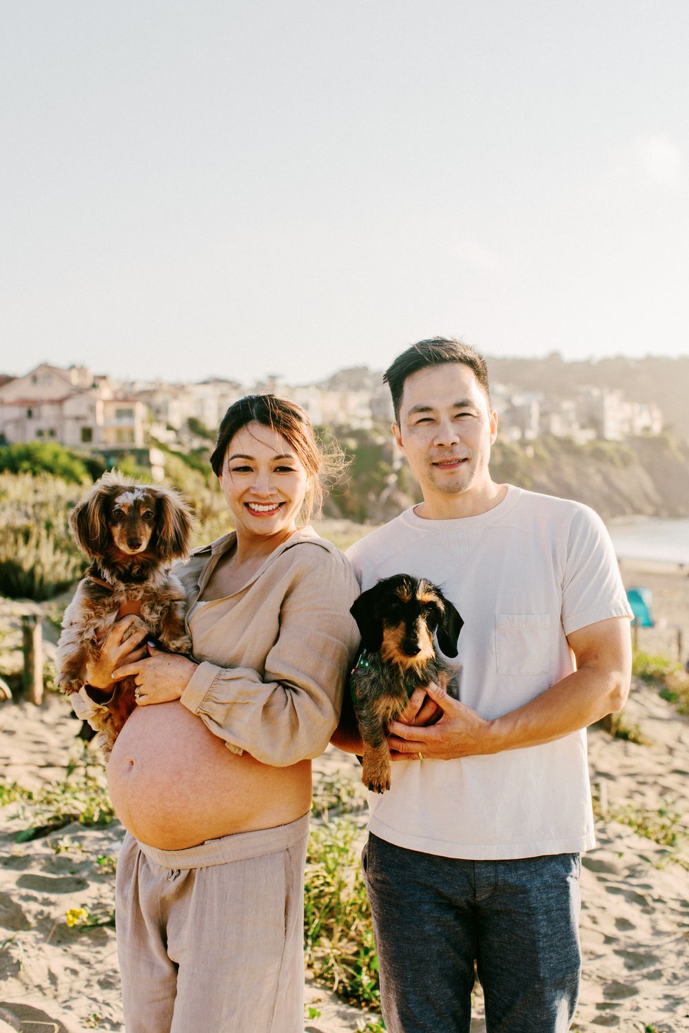 Happy couple holding two small dachshund dogs on sunny beach overlook.
