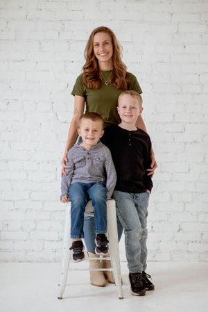 Family portrait against white brick wall with children sitting and standing on white stool.