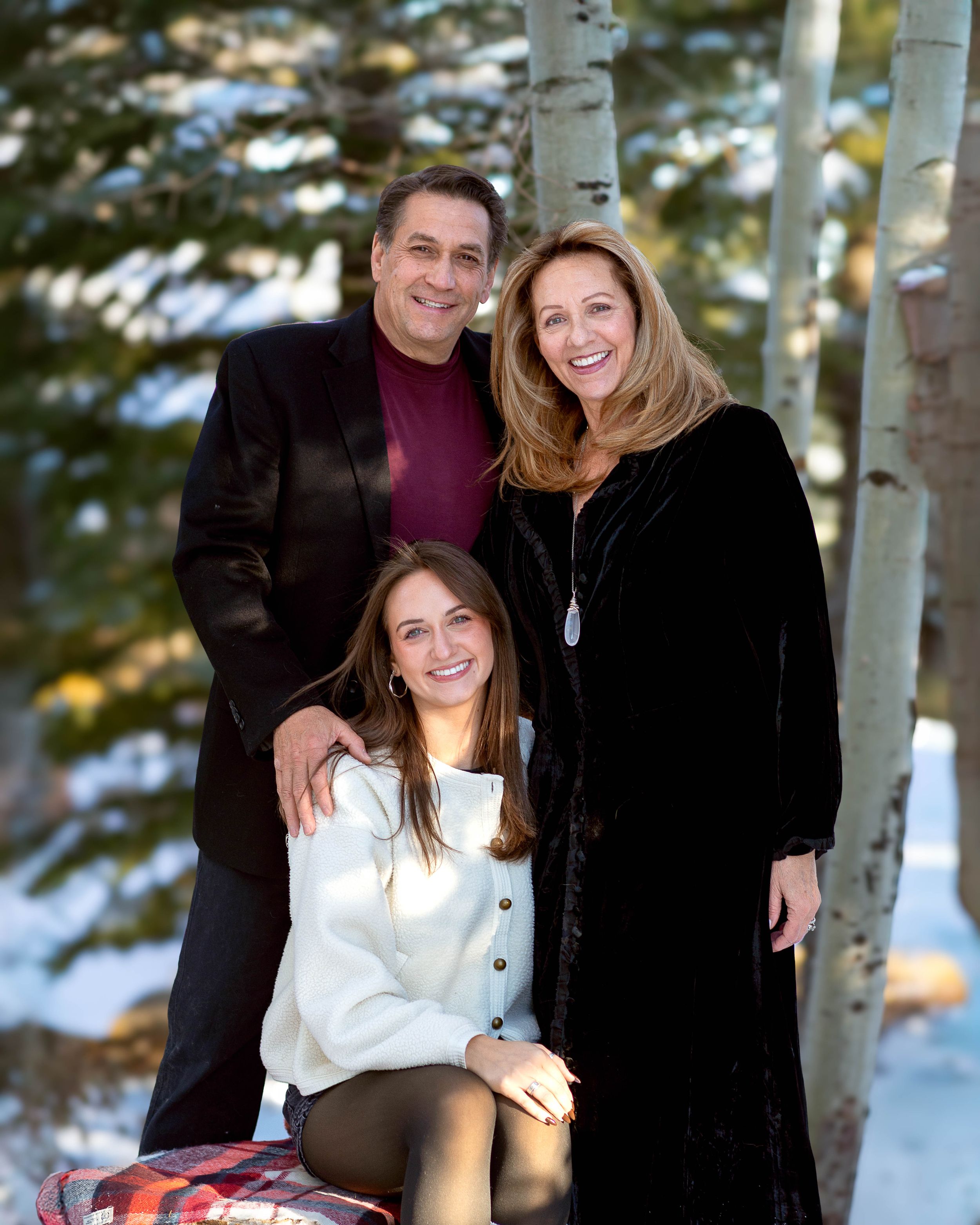 A winter family portrait with aspen trees and snow in the background.