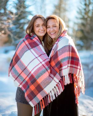 Two people wrapped in plaid blanket sharing laughter in winter setting.