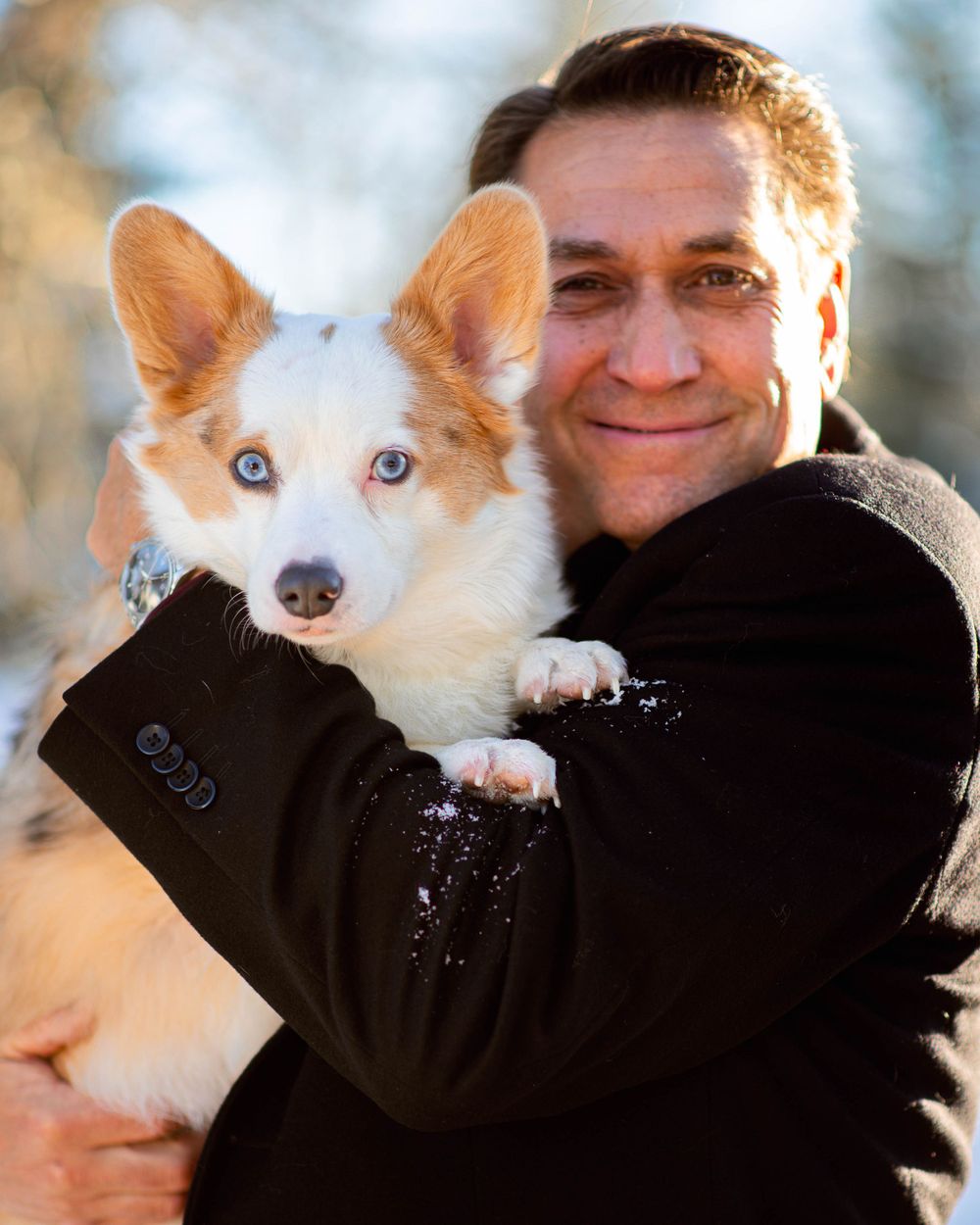 Corgi with striking blue eyes being held in winter scene.
